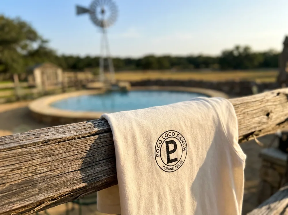 Ranch Circle tee draped on a fence rail at the windmill pool